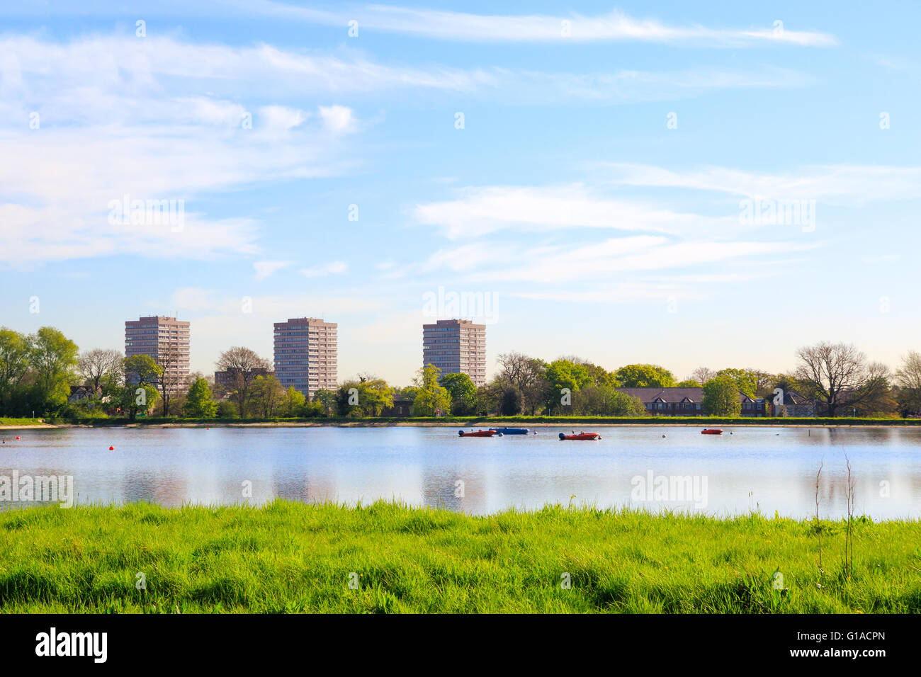 Frühlings-Blick auf Stoke Newington West Reservoir, Hackney, London mit grünen Rasen, blauer Himmel und ein paar schwimmende Boote Stockfoto