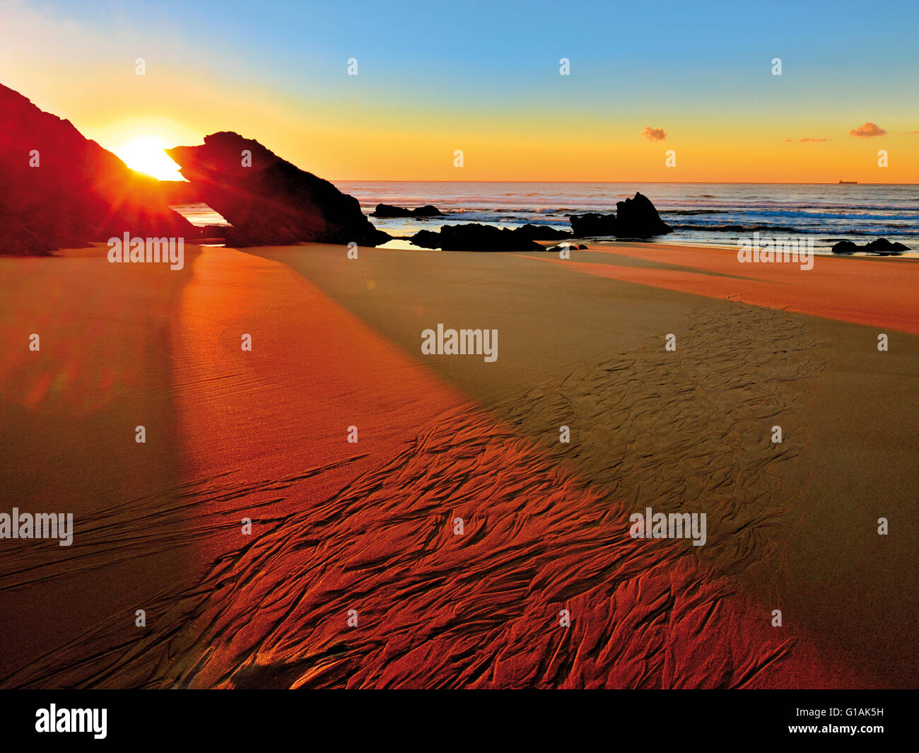Portugal, Alentejo: Letzte Sonnenlicht Eingabe zwischen zwei Felsen leuchtenden nassen Sand am Strand bei Ebbe Stockfoto