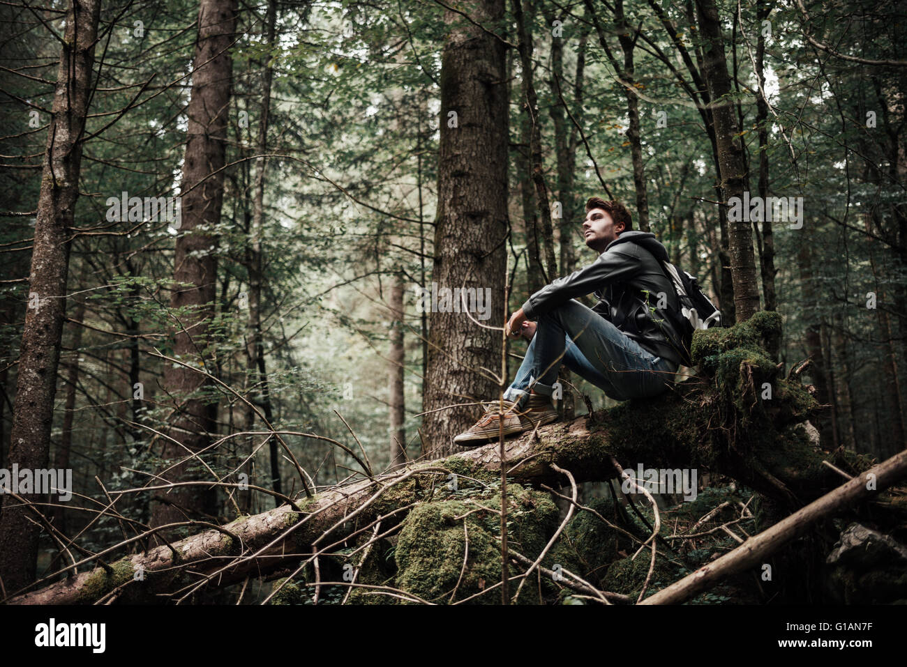 Junger Mann auf einem Baumstamm im Walde sitzen und entspannen, Freiheit und Individualität Konzept Stockfoto