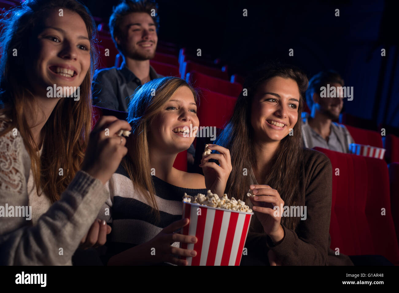 Lächelnde junge Mädchen im Kino sitzen, einen Film und Essen Popcorn, Freundschaft und Entertainment-Konzept Stockfoto