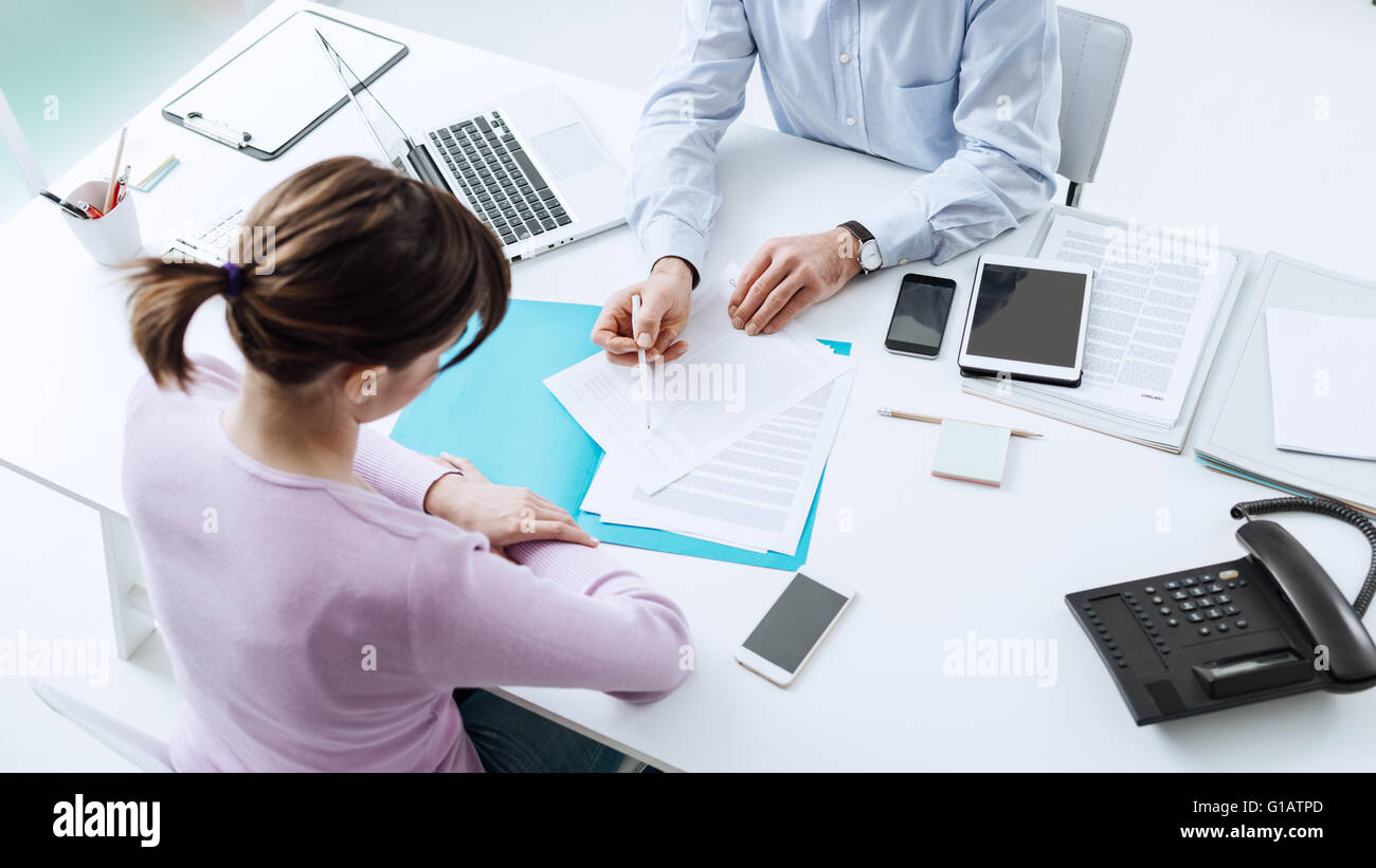 Berater treffen mit einem Kunden in sein Büro, er erklärt ein Vertragsdokument und Politik, die Frau sitzt an seinem Schreibtisch Stockfoto