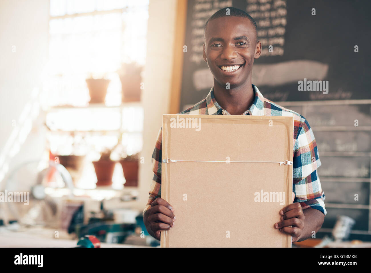 Junge Unternehmer afrikanischer Abstammung stolz lächelnd in die Kamera halten Sie einen Bilderrahmen, in seinem eigenen Pi gemacht wurde Stockfoto