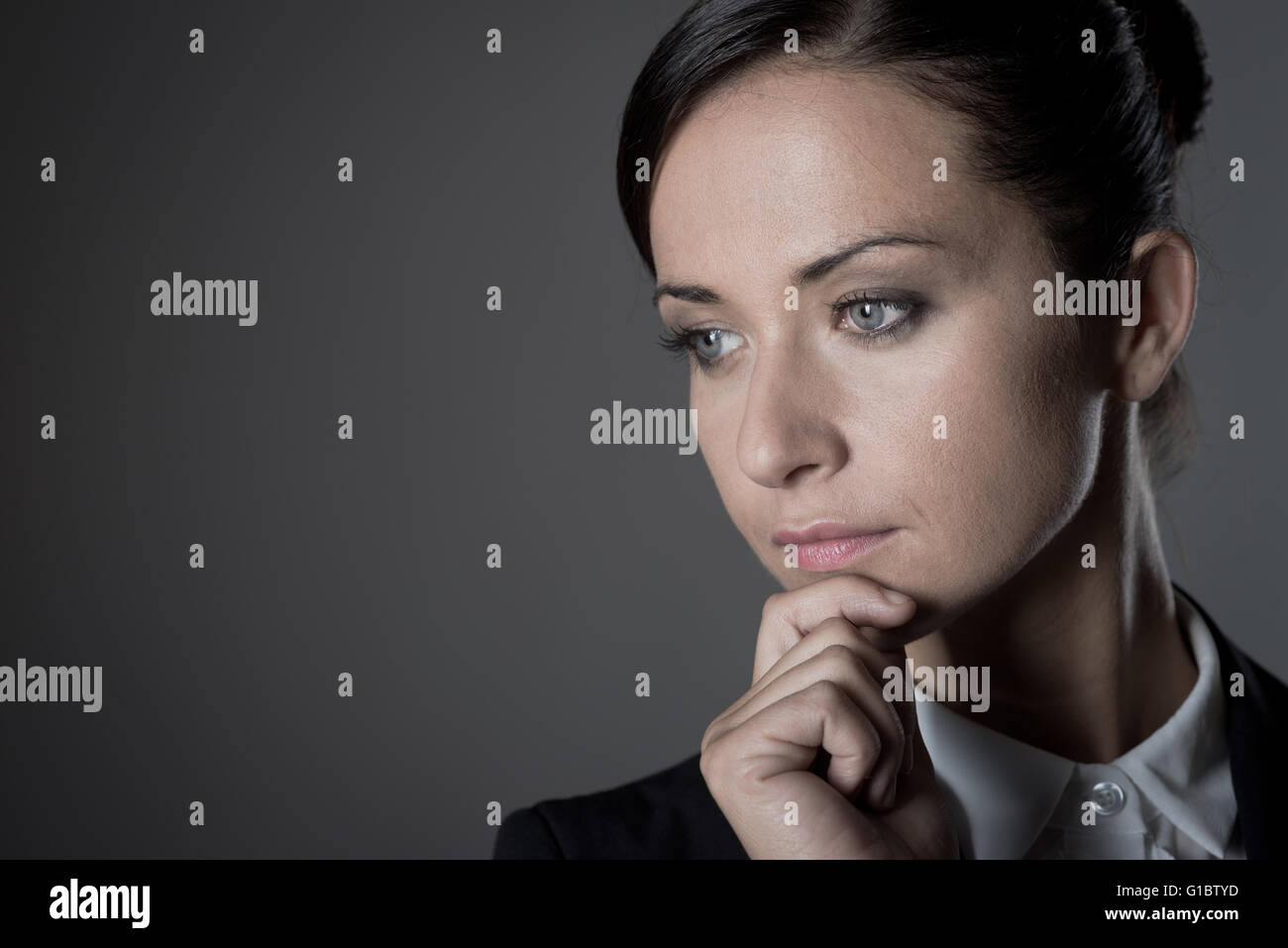 Junge attraktive Geschäftsfrau auf dunklem Hintergrund denken mit Hand am Kinn. Stockfoto