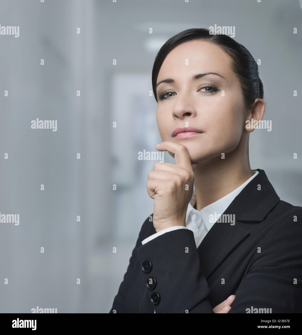 Zuversichtlich, charmante weibliche Manager mit Hand am Kinn posiert auf grauem Hintergrund. Stockfoto