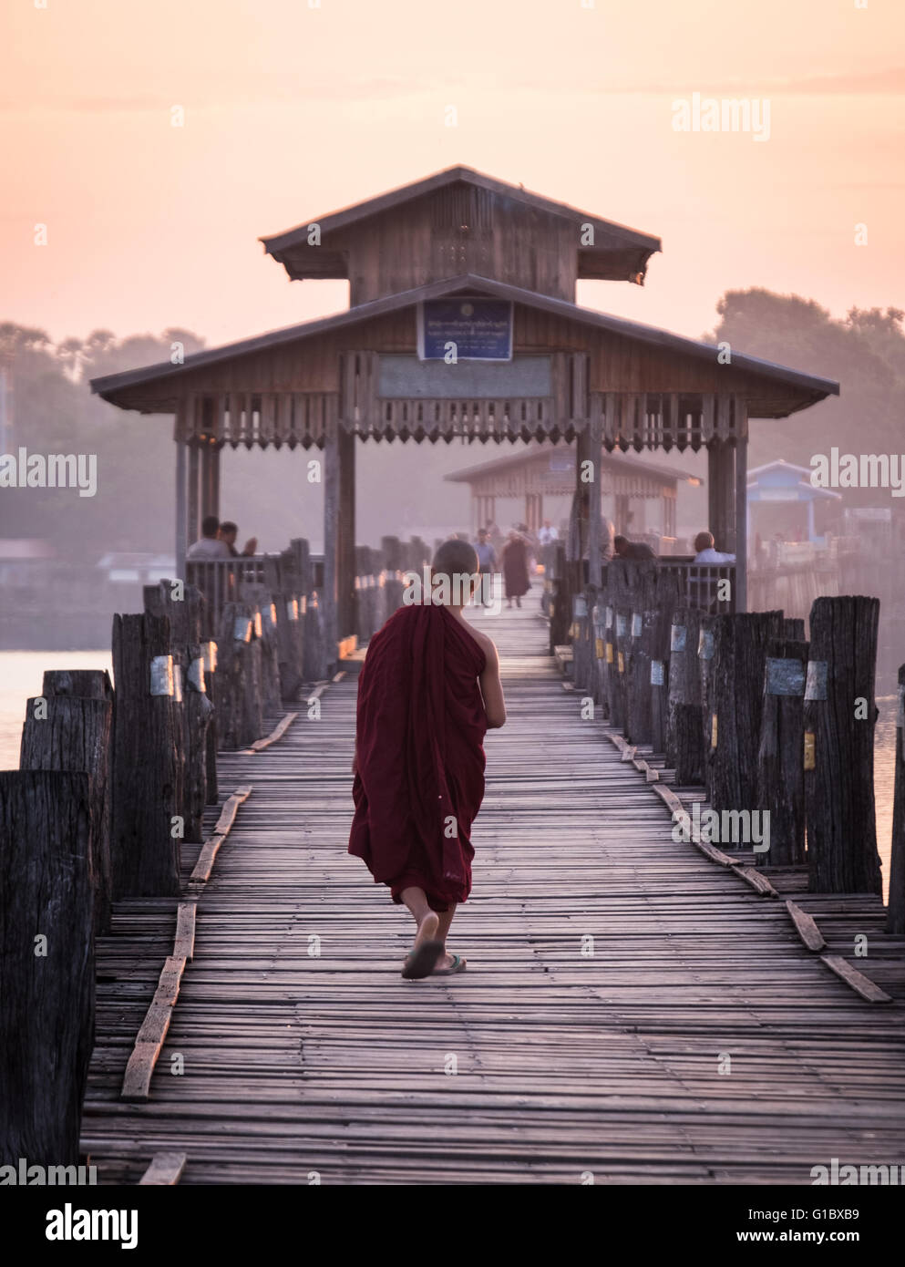 Ein junger Novize Wanderungen bei Sonnenaufgang über der hölzernen U Bein Brücke in der Nähe von Amapura in Mandalay. Stockfoto