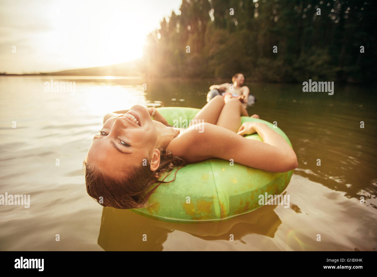 Closeup Portrait lächelnd junges Mädchen in einem Innertube mit einem Mann im Hintergrund in einem See schweben. Junge Frau Entspannung in Stockfoto