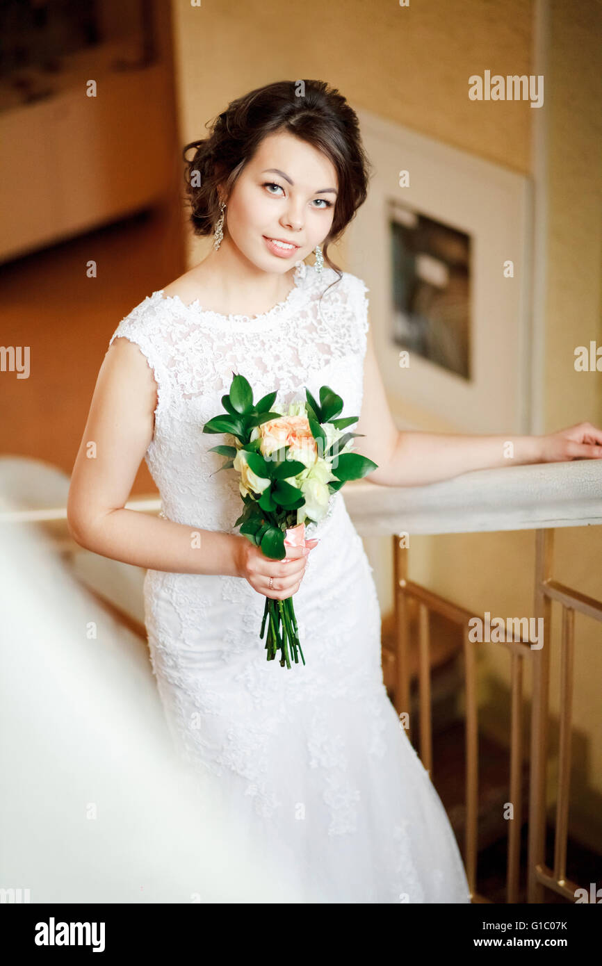 Schöne Braut mit Brautstrauß geht die Treppe hinauf, im Innenbereich. Stockfoto