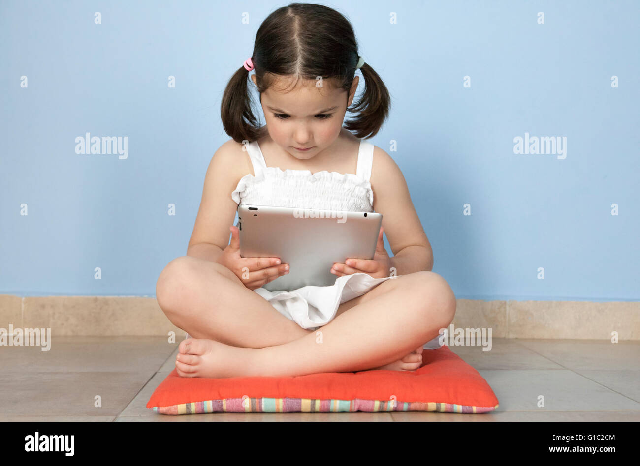 Kleines Mädchen sitzt in ihrem Stockwerk mit Tablet-PC Stockfoto