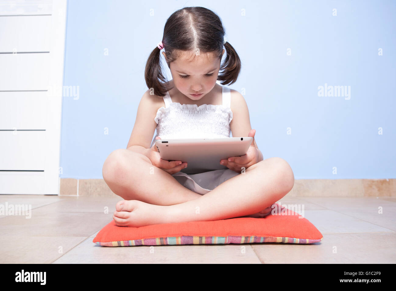 Kleines Mädchen sitzt in ihrem Stockwerk mit Tablet-PC Stockfoto