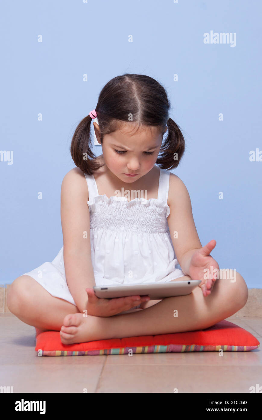 Kleines Mädchen sitzt auf ihr Stockwerk mit Tablet-PC Stockfoto