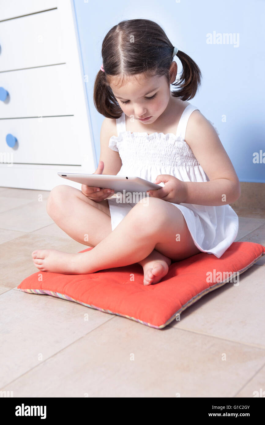 Kleines Mädchen sitzt auf ihr Stockwerk mit Tablet-PC Stockfoto