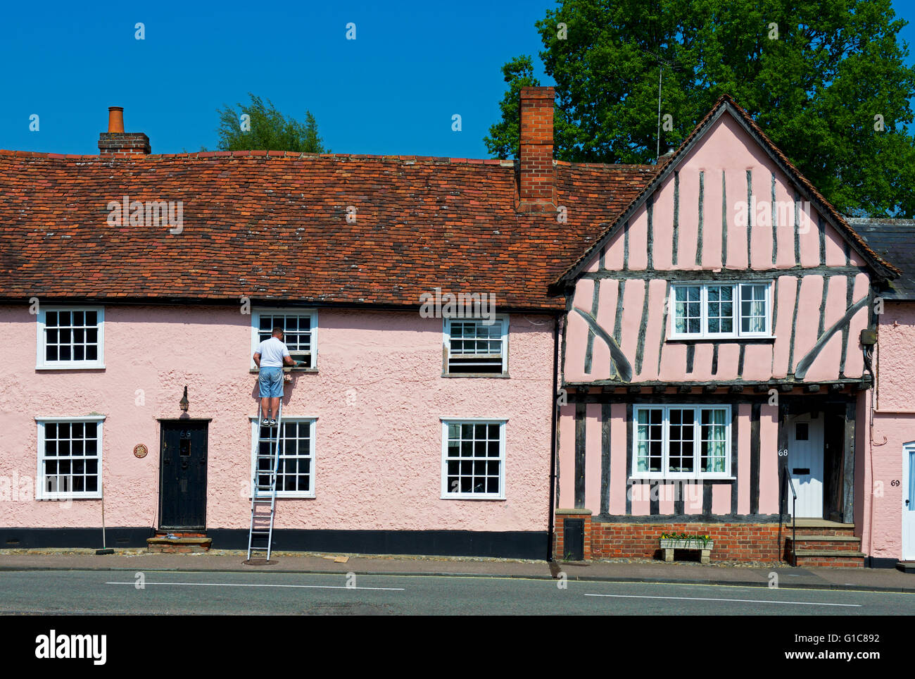 Mann auf Leiter, Reparatur von Fensterrahmen Haus im Dorf Lavenham, Suffolk, England UK Stockfoto