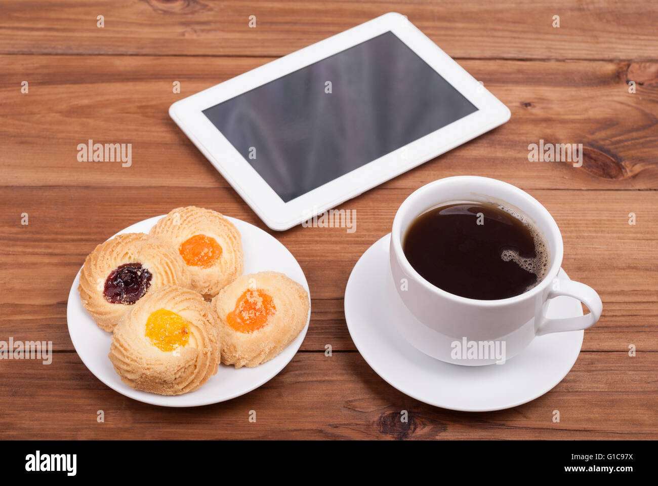 Tasse Kaffee und süße Kuchen-digital-Tablette auf dem Tisch. Stockfoto