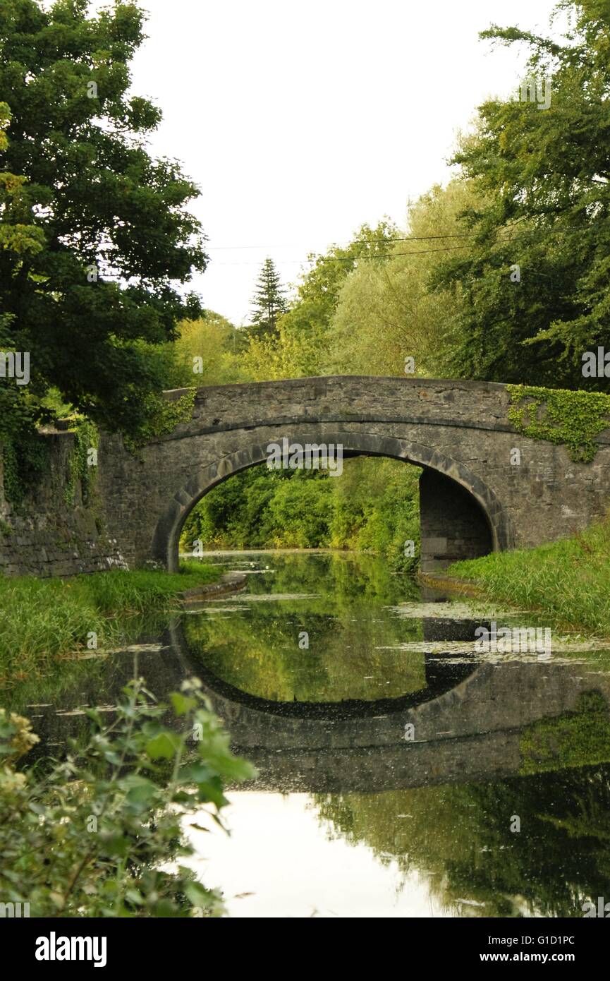 Alte Steinbrücke über einen Kanal in Irland, reflektiert in den Fluss Stockfoto
