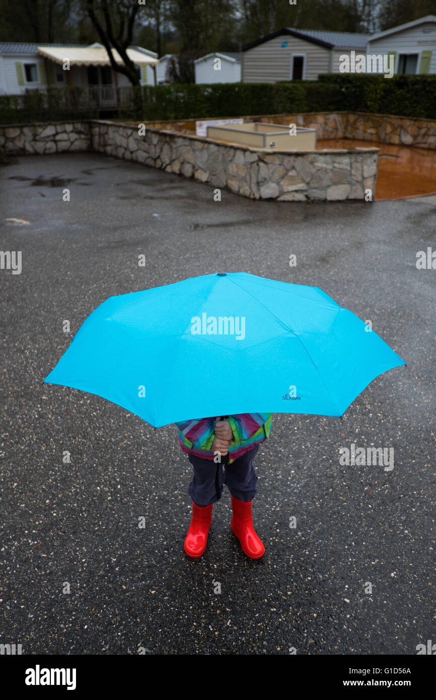 Kind mit Gummistiefeln und Regenschirm im Regen auf einem Campingplatz im April, Frankreich Stockfoto