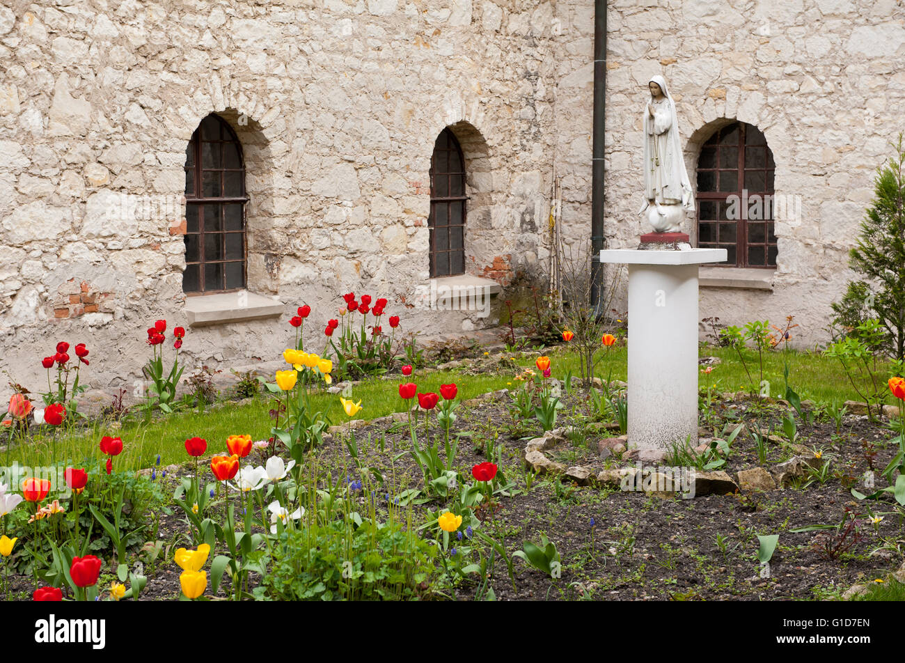 Heilige Mutter Denkmal im Viereck umgeben von Kloster Wände mit Fenstern, klösterliche Lustgarten mit blühenden Tulpen. Stockfoto