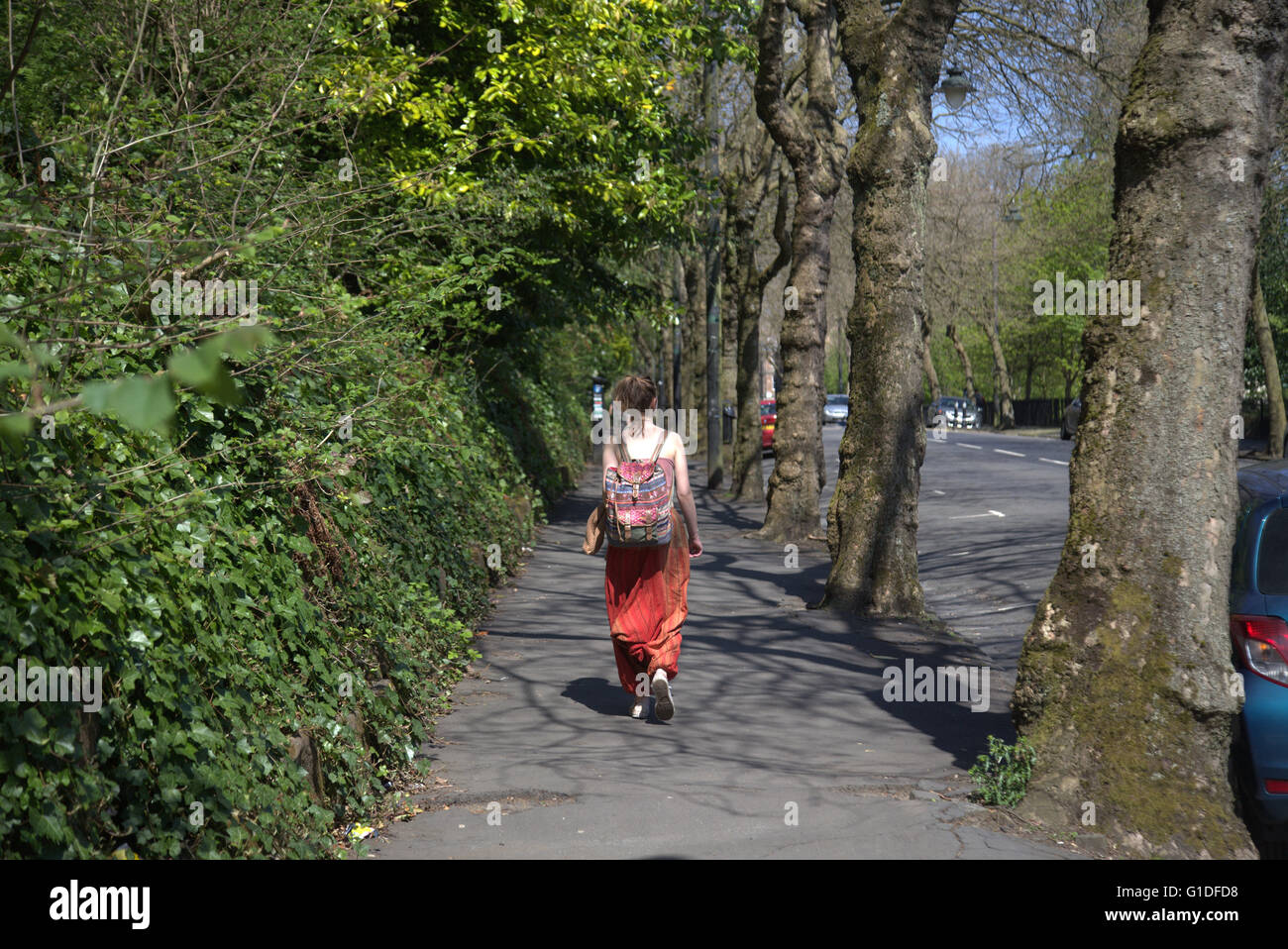 attraktiv gekleidete junge Frau in hellen Farben mit Rucksack Kelvingrove Park, Glasgow, Schottland, Großbritannien. Stockfoto