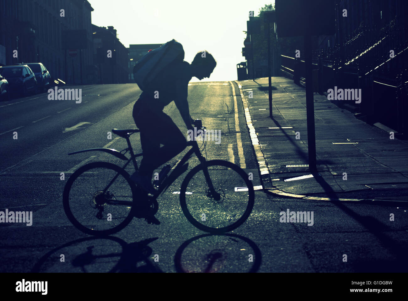 Silhouette des Jünglings auf Fahrrad auf Glasgow Straße mit Straße Contre-Jour Hintergrundbeleuchtung in Glasgow, Schottland, Großbritannien. Stockfoto