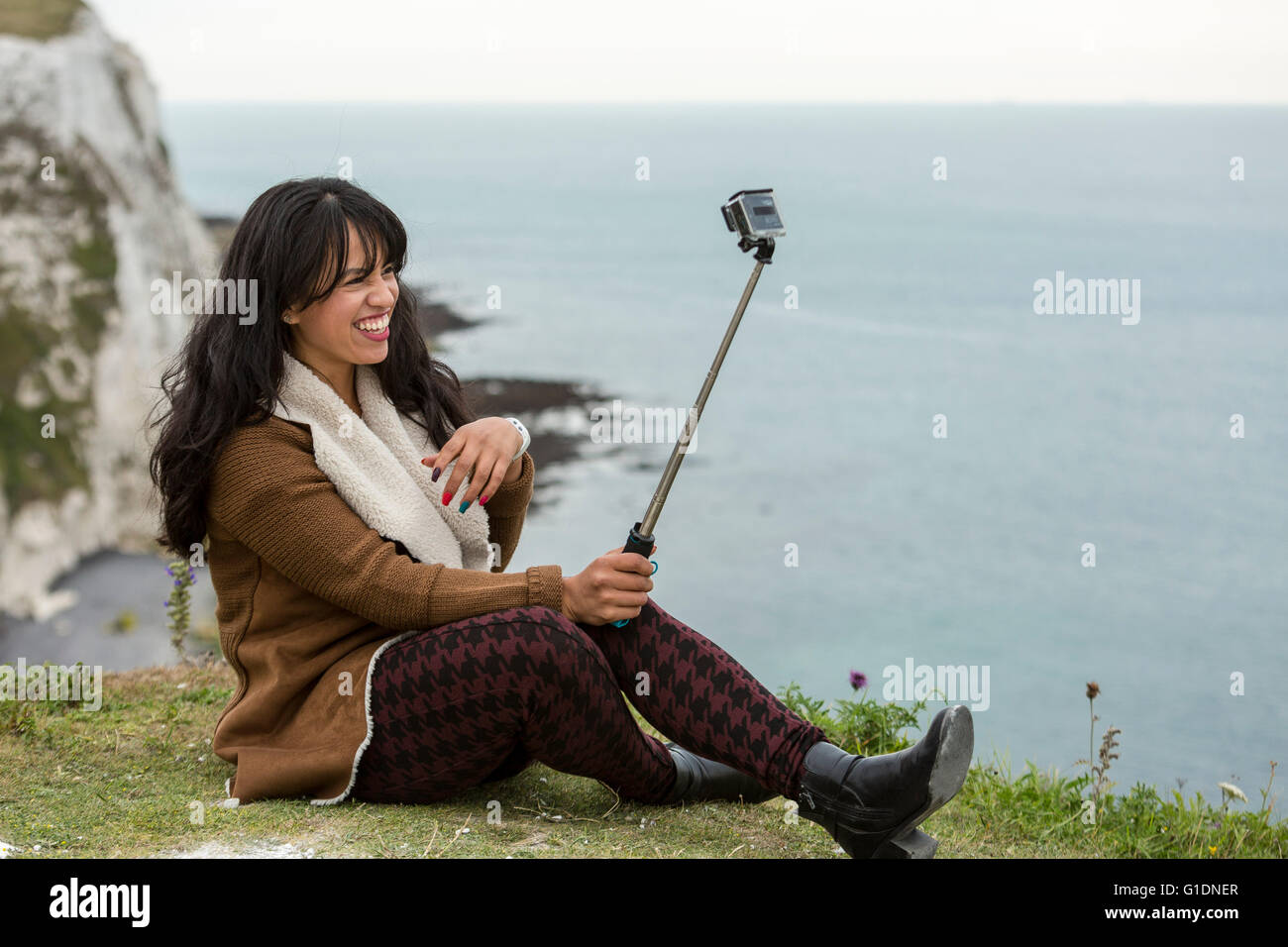 Junge Frau, die eine Selfie mit einer GoPro-Kamera und einem Selfie-Stick. Die weißen Klippen von Dover, Dover, Kent, Großbritannien Stockfoto