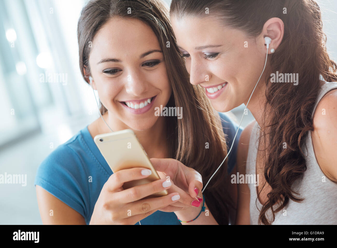 Ziemlich lächelnde junge Mädchen teilen Kopfhörer und Musikhören mit einem Smartphone Stockfoto