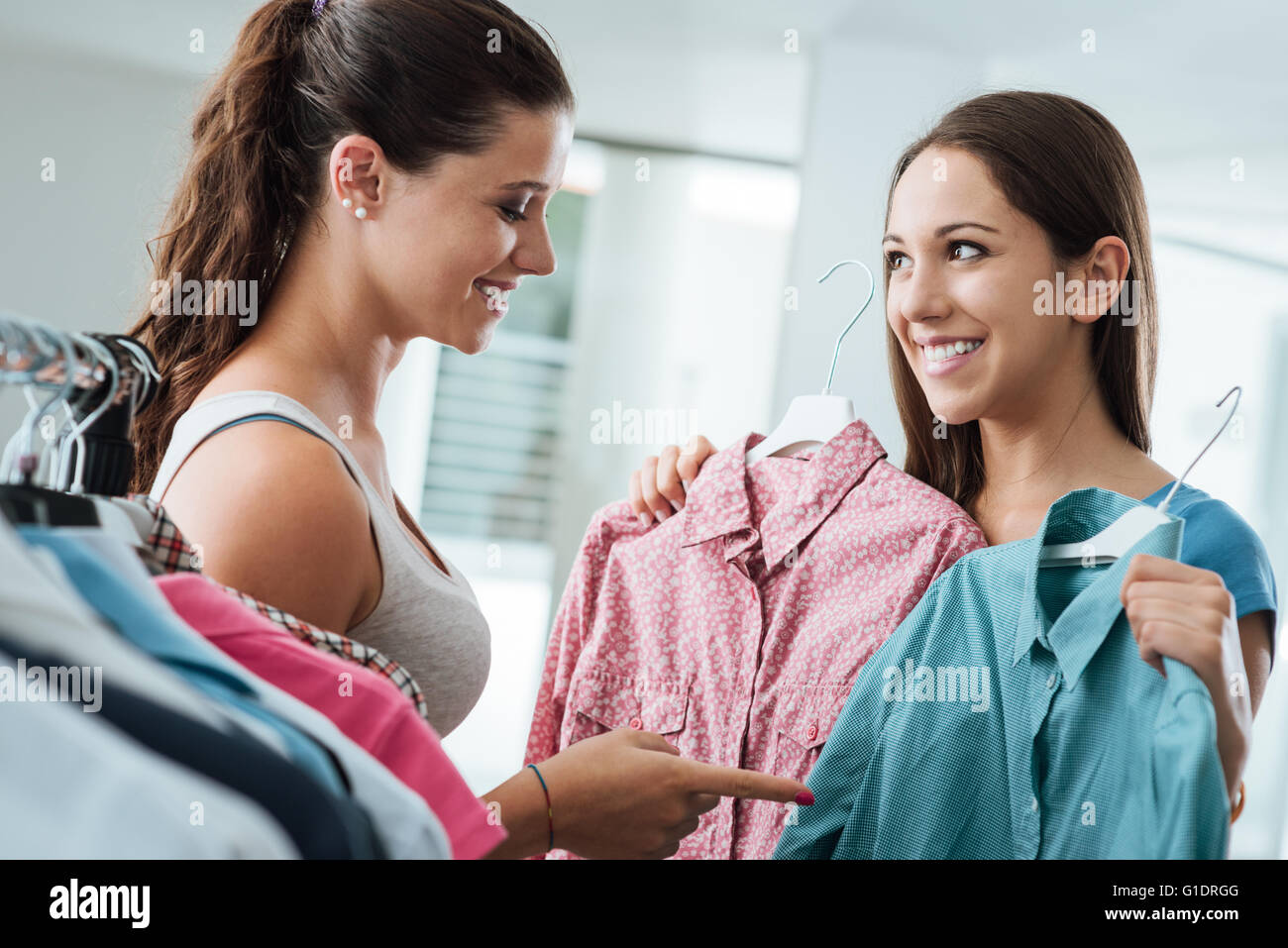 Mädchen Einkaufen eine Auswahl ein Hemd im Laden, eine junge Verkäuferin lächelnd hilft ihr Stockfoto