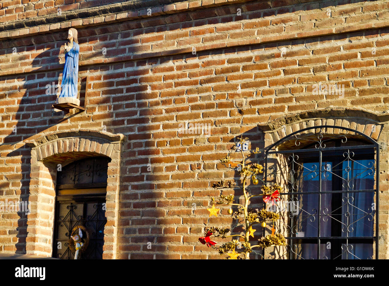 Rustikale roten Backsteinmauer mit Statuette eines Heiligen und Rundbogenfenster mit Eisen Tiefenbilder in Todos Santos, Baja, Mexiko. Stockfoto