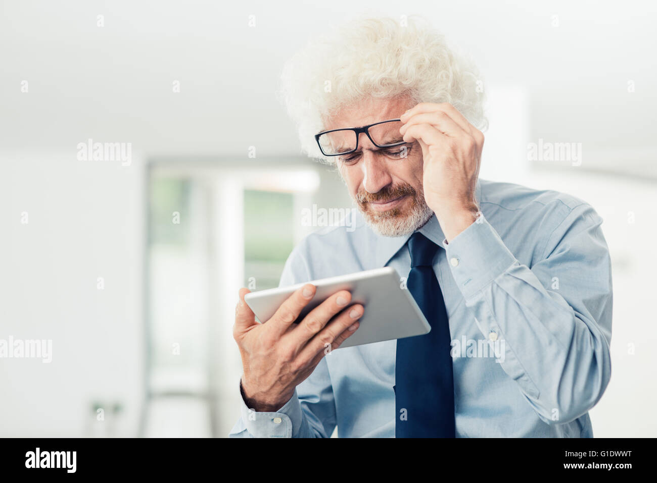 Unternehmer haben Sehprobleme, er nutzt eine Tablette und Anpassung seiner Brille, Büroeinrichtung auf Hintergrund Stockfoto