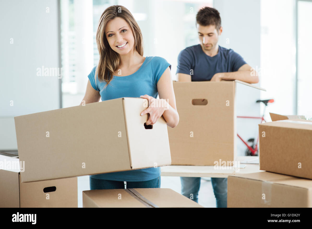 Junge glückliche Paar Umzug in ihr neues Haus und Kisten auspacken, sie tragen einen Karton und lächelt in die Kamera Stockfoto