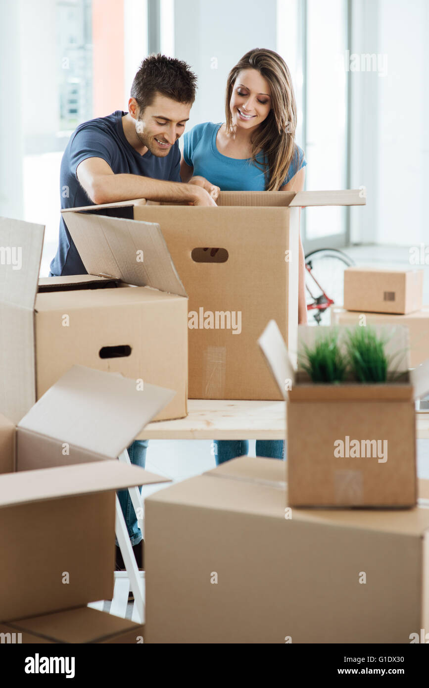 Lächelnd junges Paar Auspacken der Kartons in einem neuen Haus, sucht Objekte in einer großen Kiste auf dem Tisch er Stockfoto