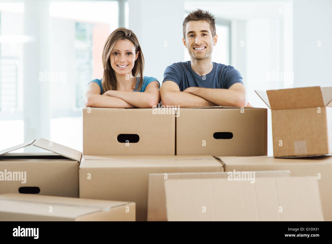 Junges Paar posiert mit Arme gekreuzt, stützte sich auf Kartons und lächelt in die Kamera, home Umzug Konzept Stockfoto