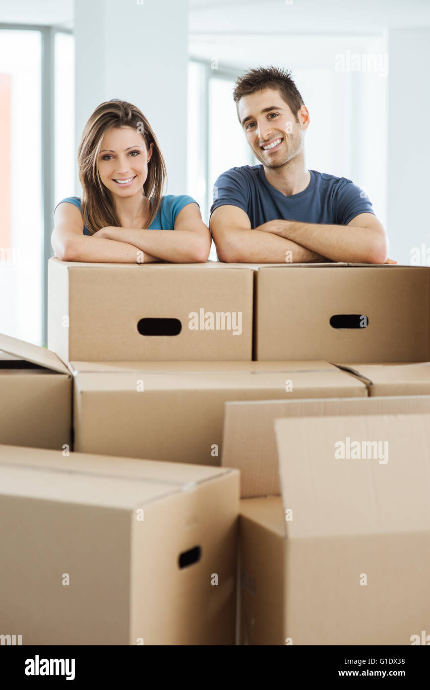 Junges Paar posiert mit Arme gekreuzt, stützte sich auf Kartons und lächelt in die Kamera, home Umzug Konzept Stockfoto