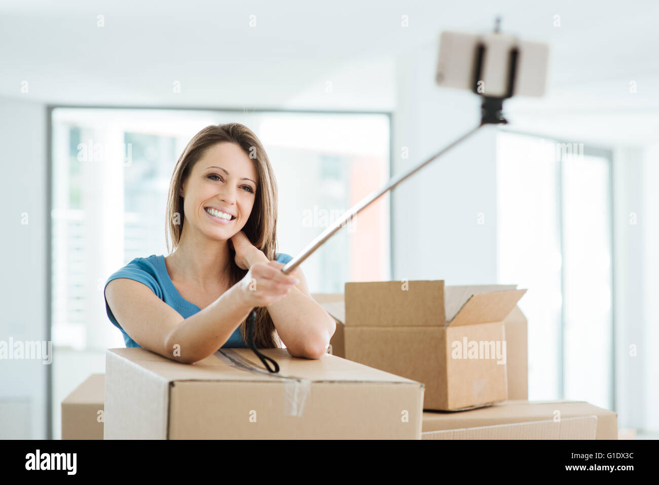 Lächelnde junge Frau bewegt sich in ihrem neuen Haus und unter Selfies mit einem Selfie-stick Stockfoto