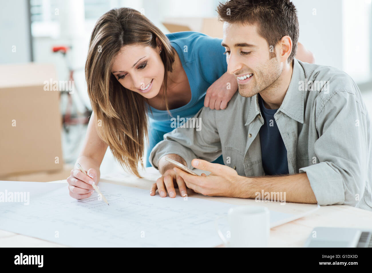 Junges Paar planen ihr neues Traumhaus, sitzt er am Schreibtisch und zeichnet sie auf ein Projekt Kartons auf Hintergrund Stockfoto