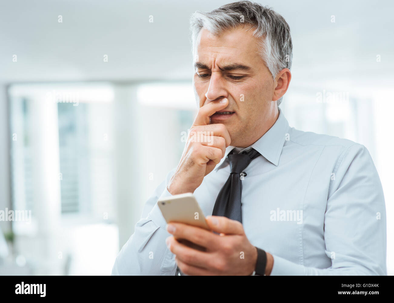 Verwirrt Geschäftsmann mit Hand am Kinn, die Probleme mit einem Smartphone Stockfoto