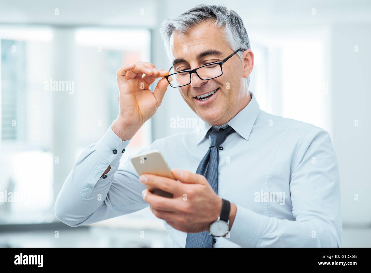 Lächelnd Geschäftsmann mit Sehprobleme, wird er seine Brille anpassen und etwas auf seinem Handy zu lesen Stockfoto
