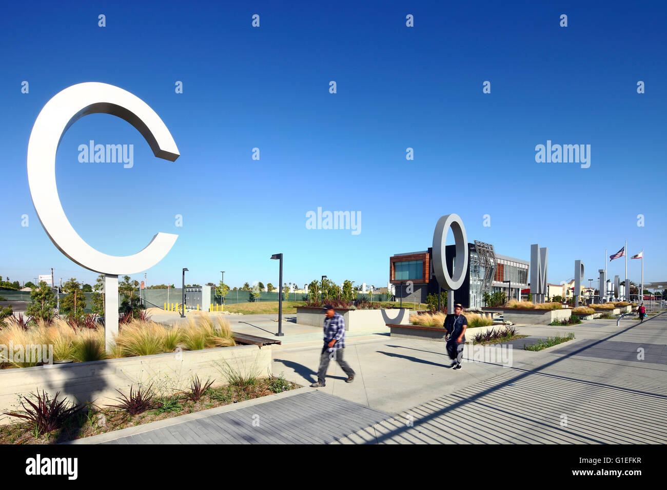Martin Luther King Jr. Transit Center, Compton, CA von Basis-Architektur. Blick auf Metall-Lettern buchstabieren Compton. Zwei Männer gehen auf Asphalt. Stockfoto