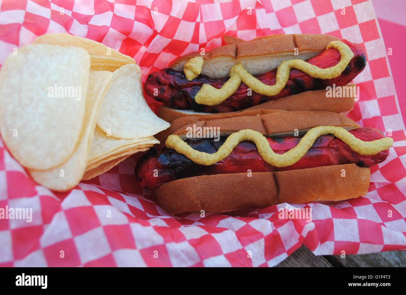 Zwei Take away Red Hot Dogs serviert mit Senf & Kartoffelchips Stockfoto