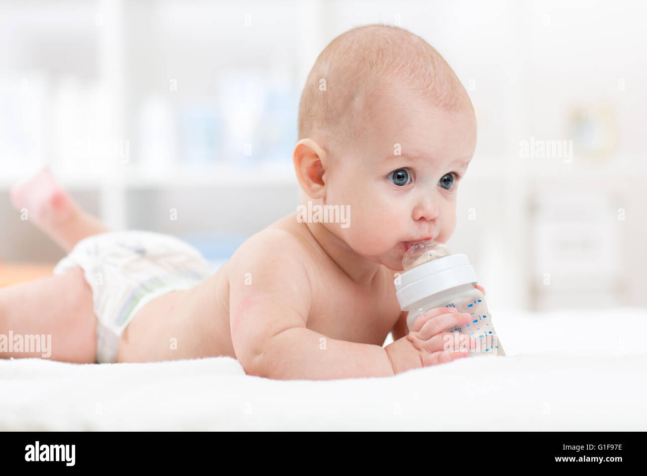 Säugling Baby trinkt Wasser aus der Flasche auf Bett liegend. Kind weared Windel im Wohnzimmer. Stockfoto