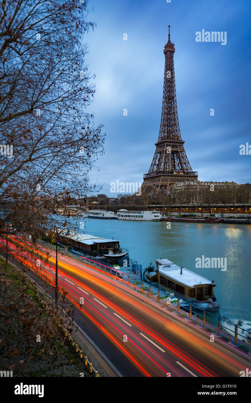 Eiffelturm in der Dämmerung an einem bewölkten Wintermorgen mit dem Seineufer und dem Auto Lichtspuren. Paris, 7. Arrondissement, Frankreich Stockfoto