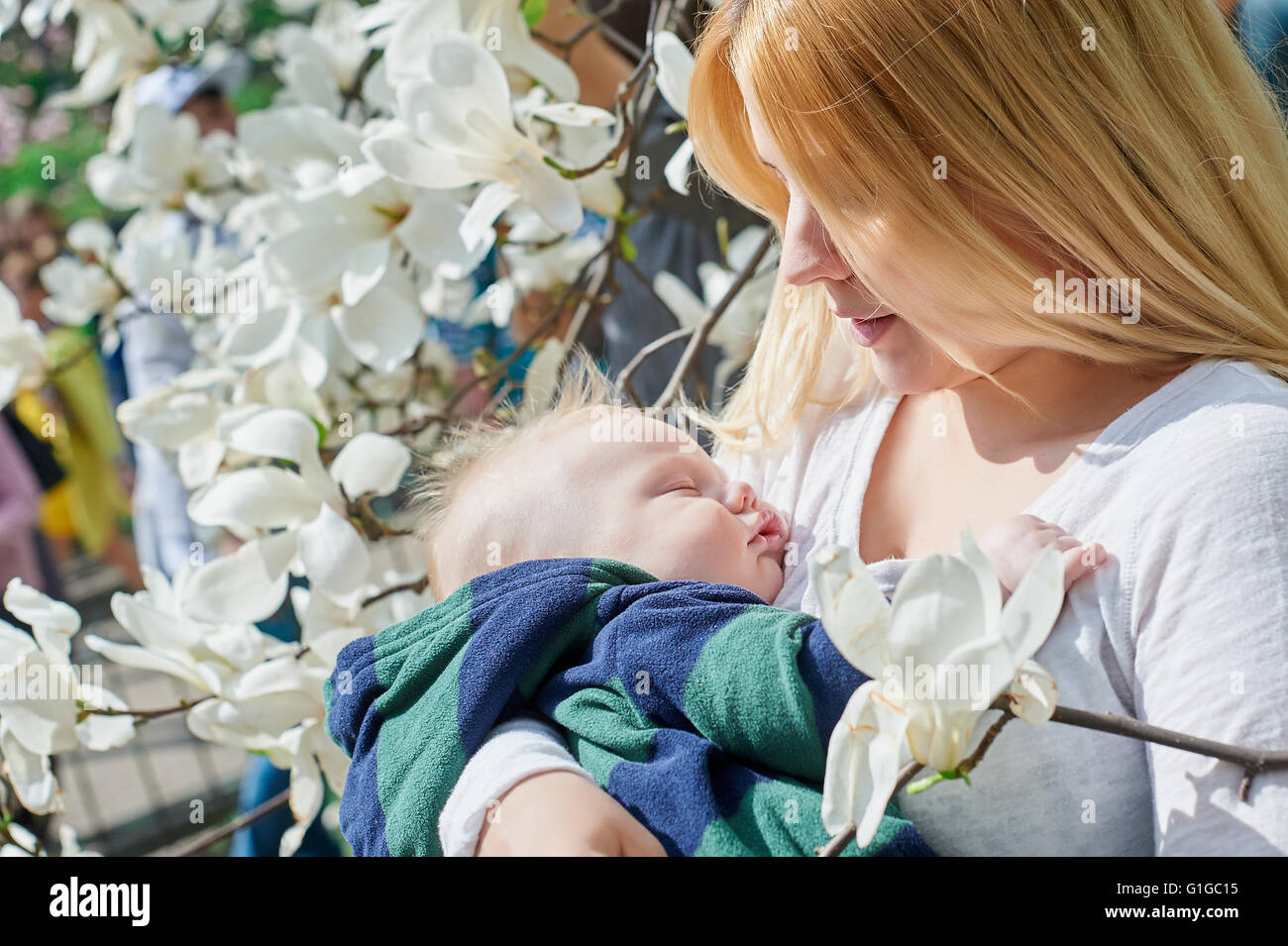 Mutter mit ihrem Baby Sohn sitzen auf Ast im Frühlingsgarten Stockfoto