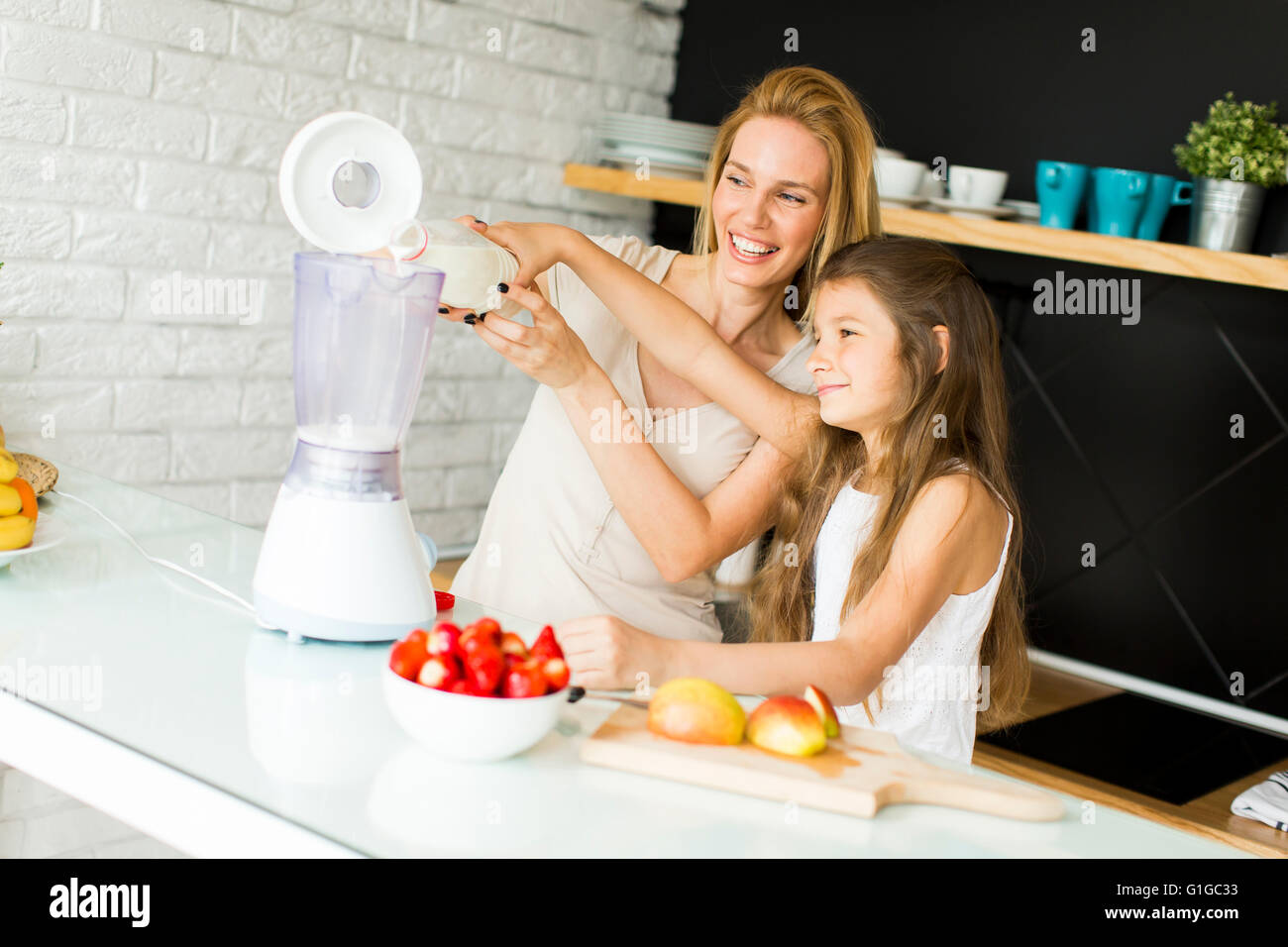 Mutter und Tochter mischen Smoothie aus frischen Früchten in der modernen Küche Stockfoto