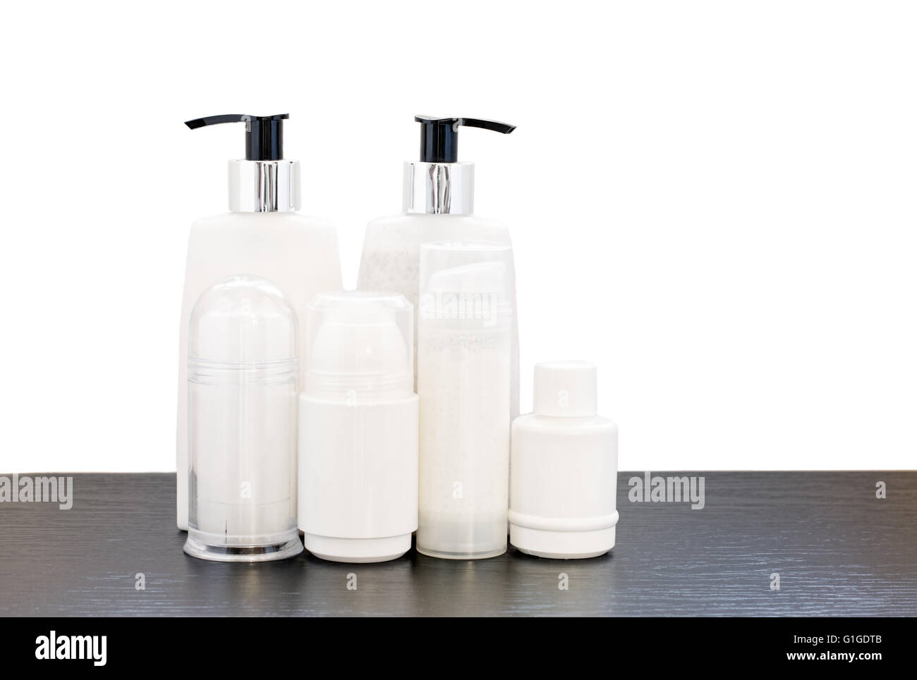 Sechs Beauty-Produkte in Plastikflaschen auf einem dunklen Holztisch mit einem weißen Hintergrund. Stockfoto