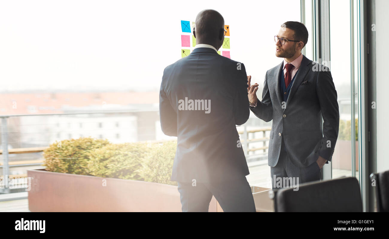 Zwei stilvolle multirassische männlichen Führungskräfte in eine rege Diskussion vor einem hellen Fenster mit Fackel und Kopie Stockfoto