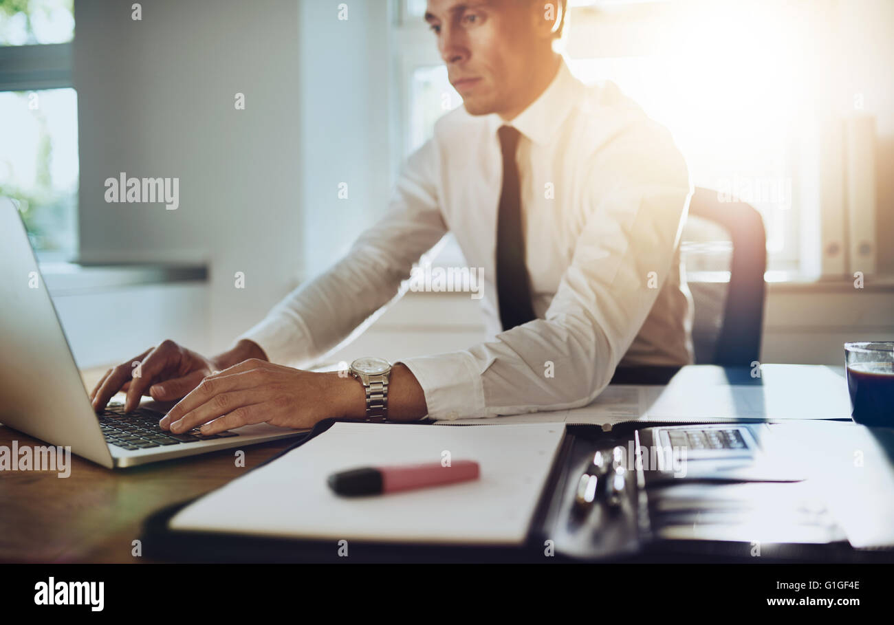 Business-Mann auf einem Laptop mit Dokumenten auf seinem Schreibtisch im Büro arbeiten tragen Anzug und Krawatte Stockfoto