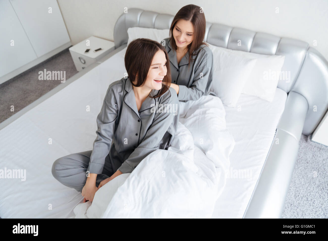 Zwei glückliche schöne junge Schwestern Zwillinge am Bett sitzen und lachen  Stockfotografie - Alamy