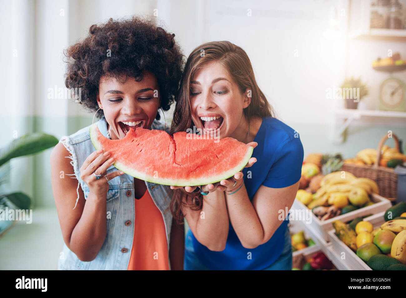 Porträt von fröhlichen jungen Frauen eine Wassermelone zum Anbeißen. Freundinnen stehen zusammen auf eine Saftbar, Essen watermelo Stockfoto