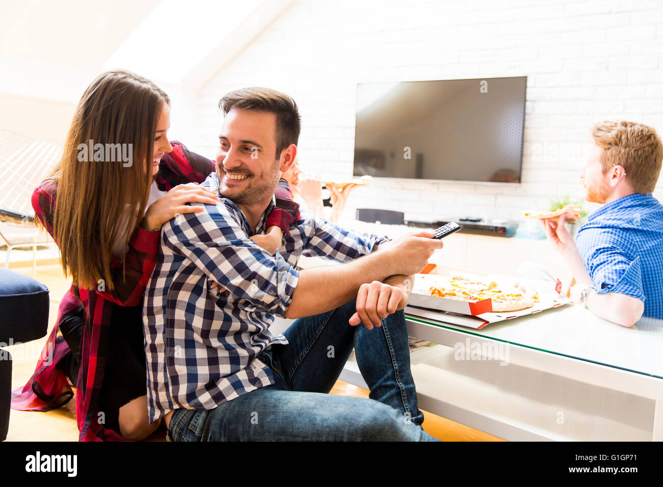 Paar Pizza essen und ein Mann, der TV-Fernbedienung Stockfoto