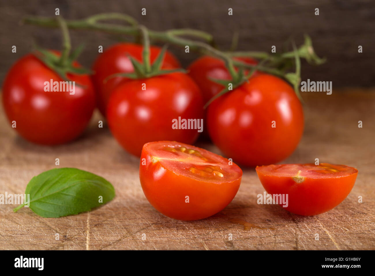 Schneiden Sie in halbe Cherry-Tomaten mit Basilikum auf Holztisch Stockfoto