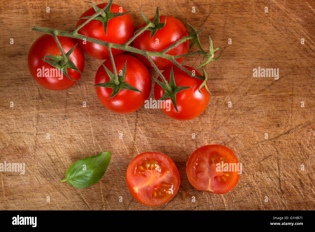 Schneiden Sie in halbe Cherry-Tomaten mit Basilikum auf Holztisch Stockfoto