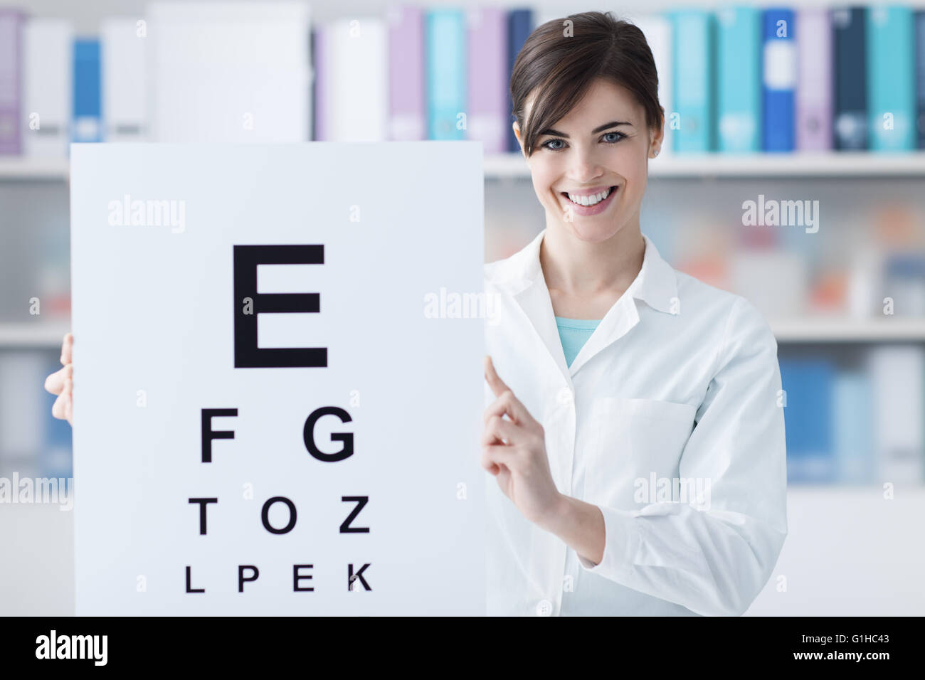 Weiblichen professionellen Augenarzt halten eine Sehtafel und lächelnd in die Kamera, ärztliche Untersuchung und Auge Pflegekonzept Stockfoto